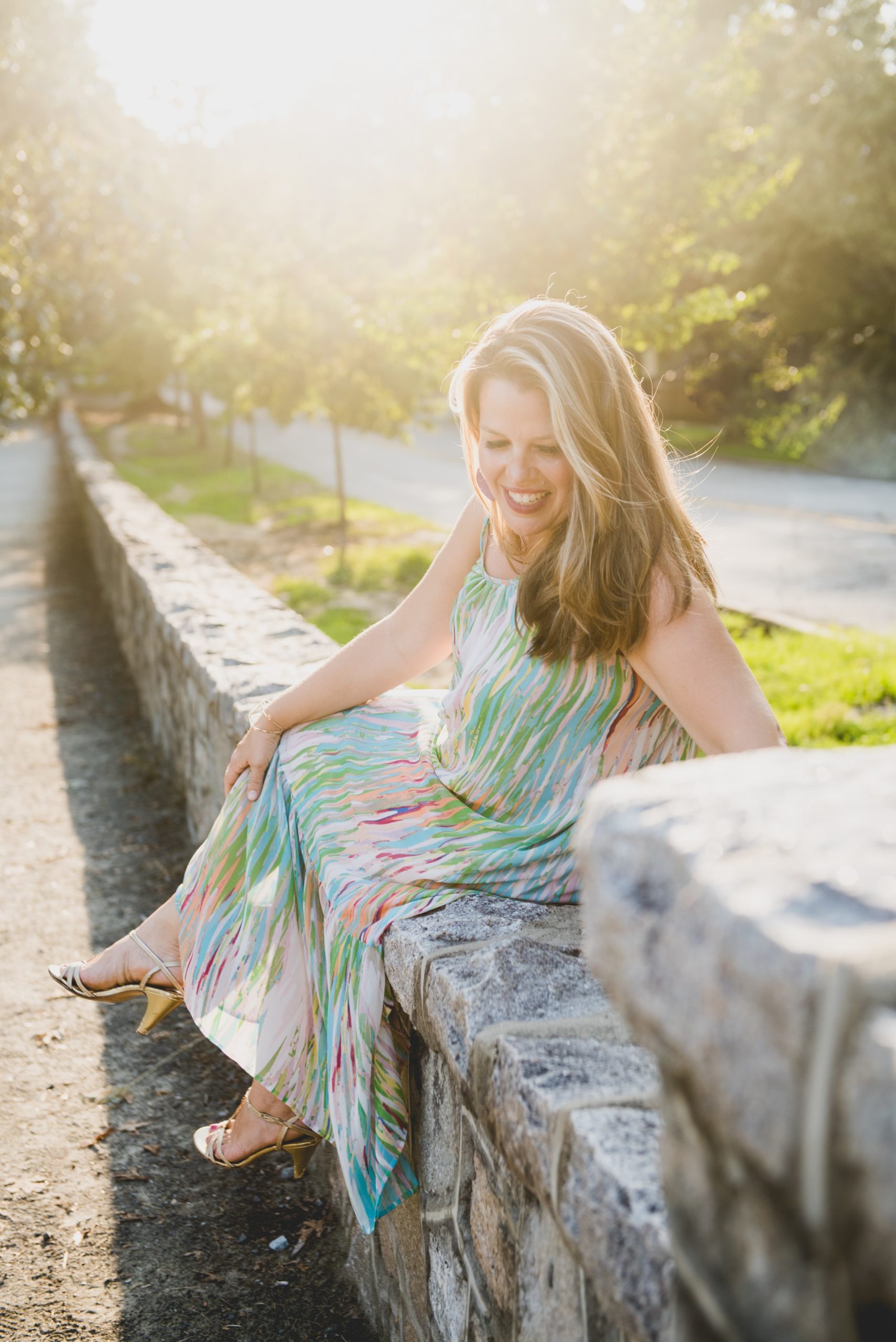 Woman with blond hair and pastel dress sitting on a rock wall outdoors